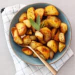 A green serving bowl of crispy herb roasted potatoes with a gold spoon.