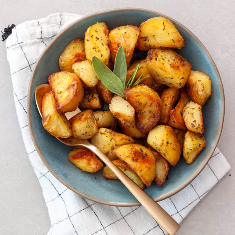 A green serving bowl of crispy herb roasted potatoes with a gold spoon.