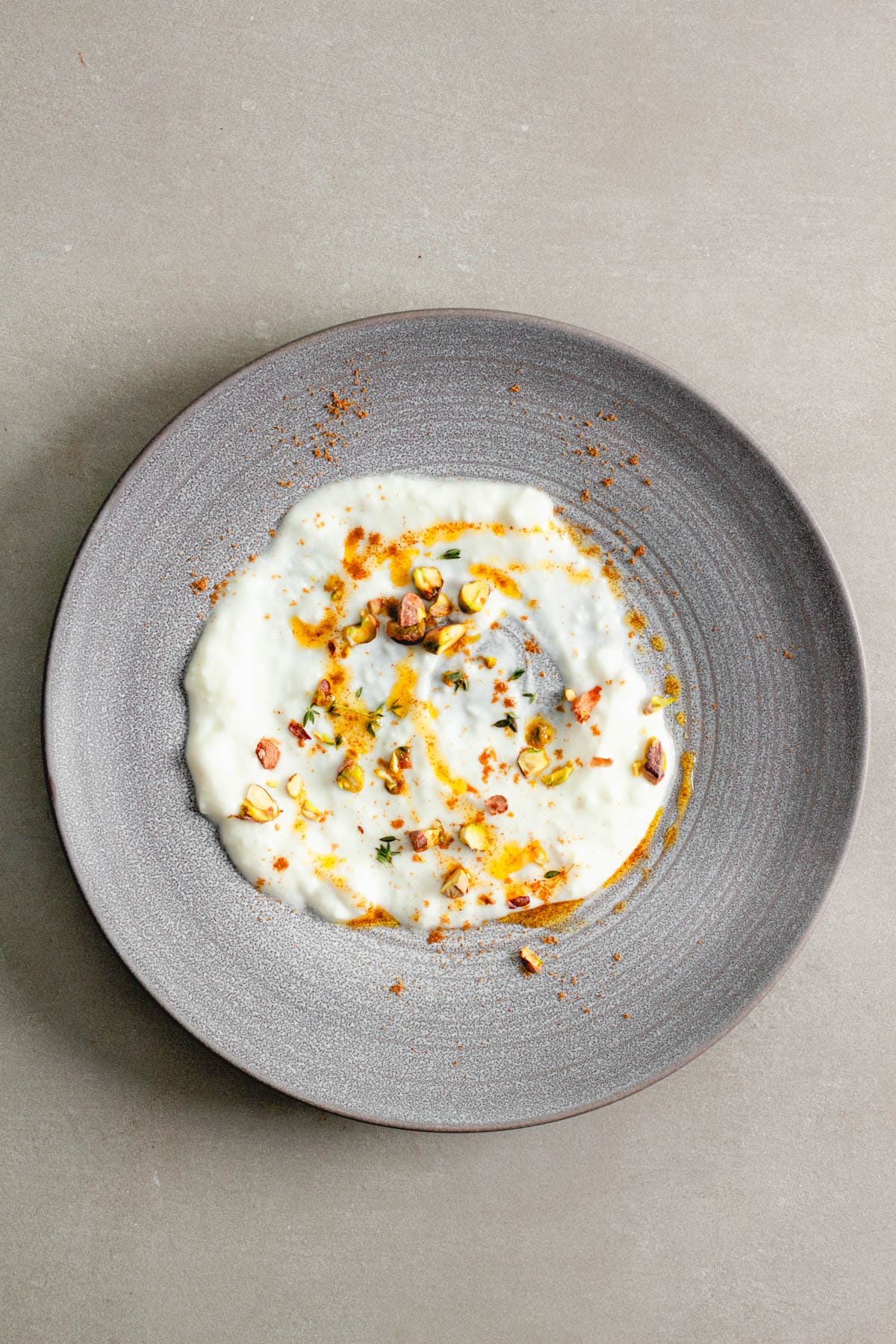 A bowl with yogurt topped with ground cumin, pistachios and olive oil.