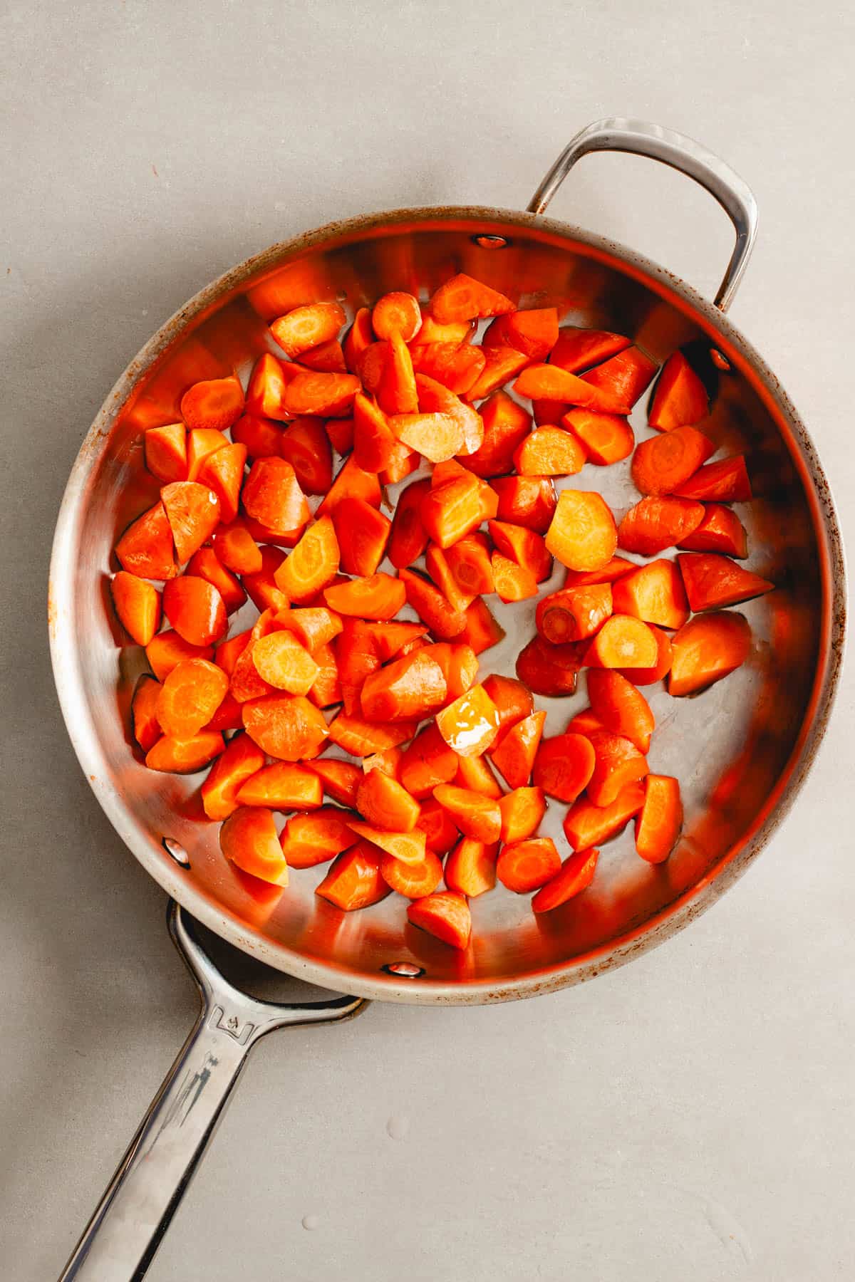 Oblong cut carrots in a large skillet with oil ready to get sauteed.