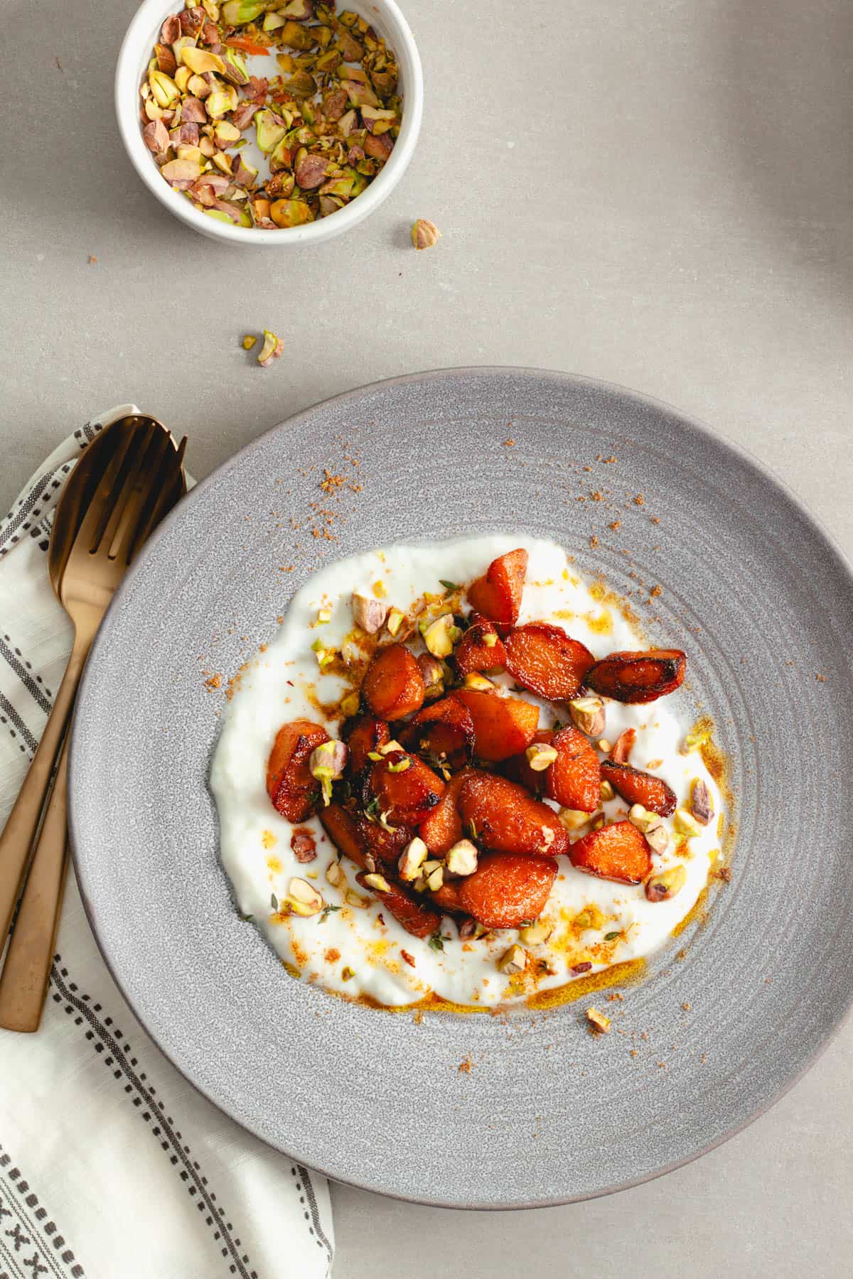 A bowl of yogurt topped with sauteed spiced carrots and pistachios.
