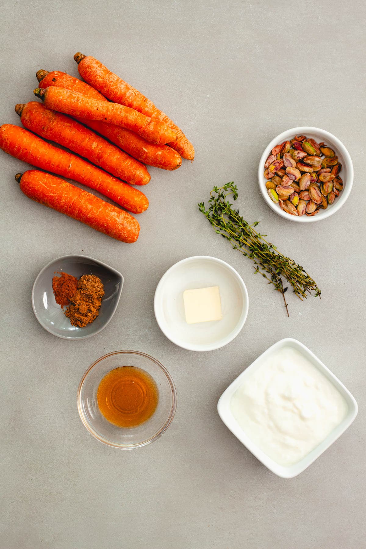 Ingredients for sauteed spiced carrots with pistachios on a gray table.
