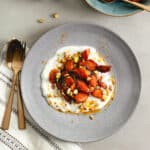 A bowl of yogurt topped with sauteed spiced carrots and pistachios.