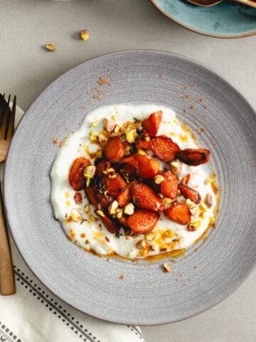 A bowl of yogurt topped with sauteed spiced carrots and pistachios.