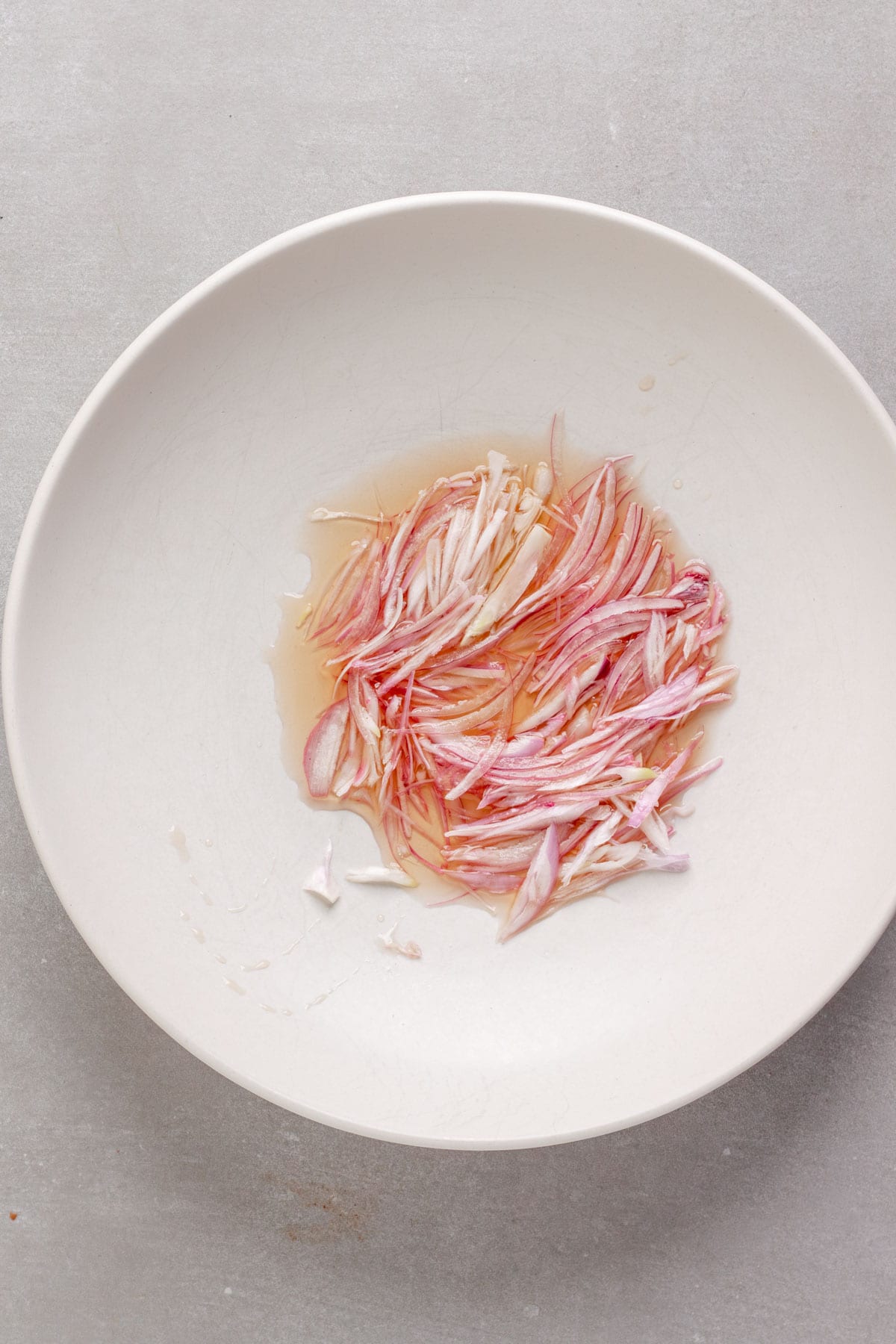 Thinly sliced shallots soaking in white balsamic vinegar in a medium bowl.