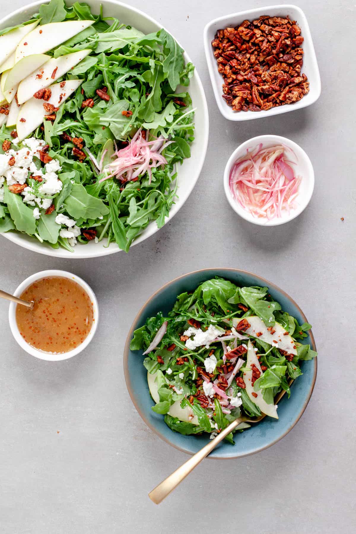 An arugula pear salad in a large bowl with a serving in a smaller blue bowl, topped with goat cheese and shallots.