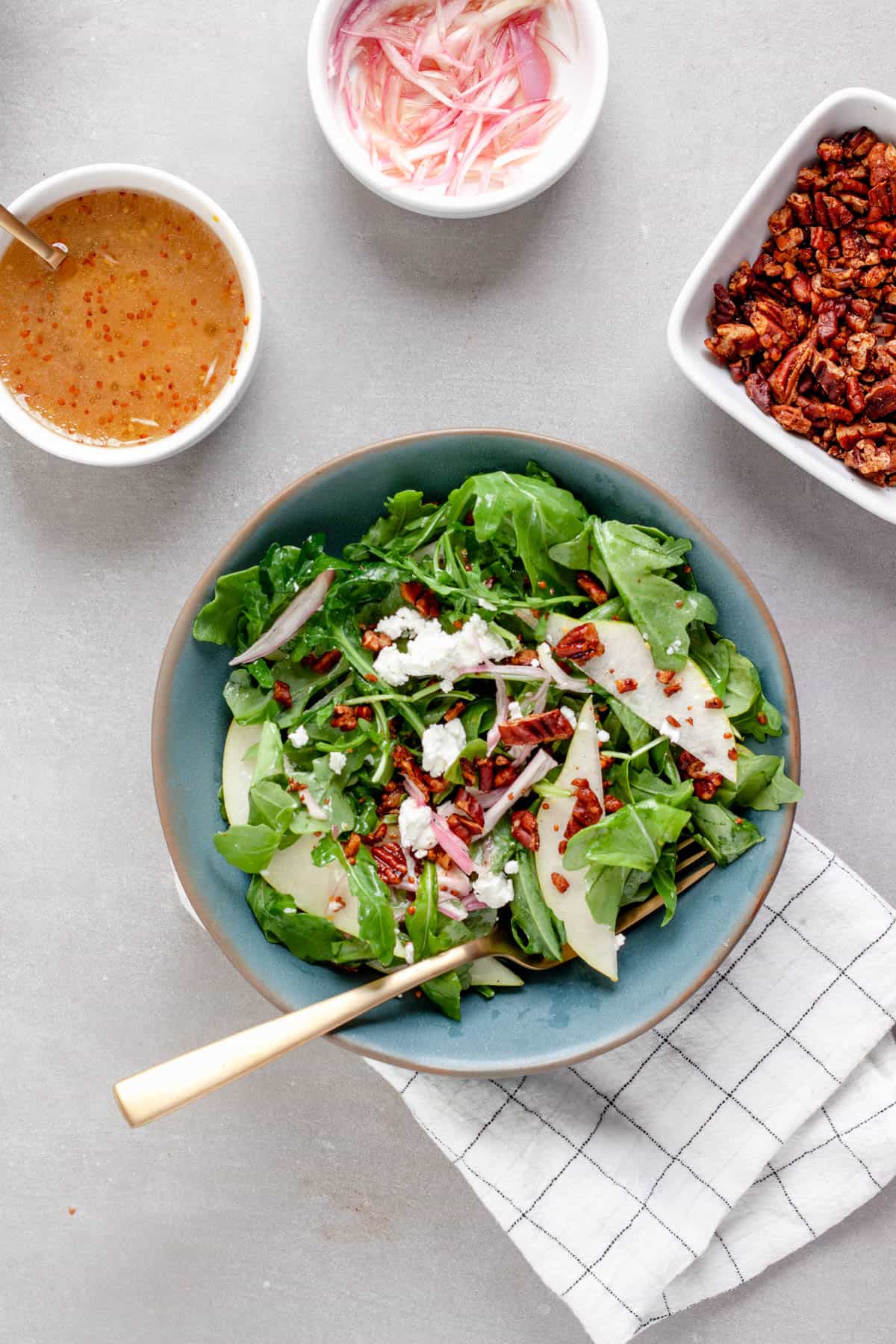 A small bowl of pear arugula salad topped with goat cheese and spiced pecans.