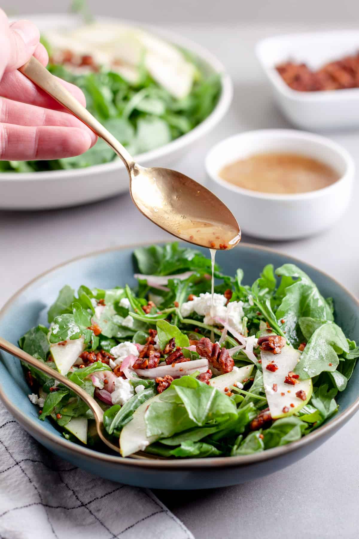 A spoonful of white balsamic vinaigrette drizzling onto a salad of arugula and pears.