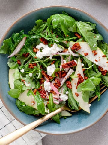 A small bowl of pear arugula salad topped with goat cheese and spiced pecans.