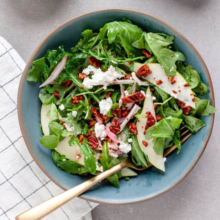 A small bowl of pear arugula salad topped with goat cheese and spiced pecans.