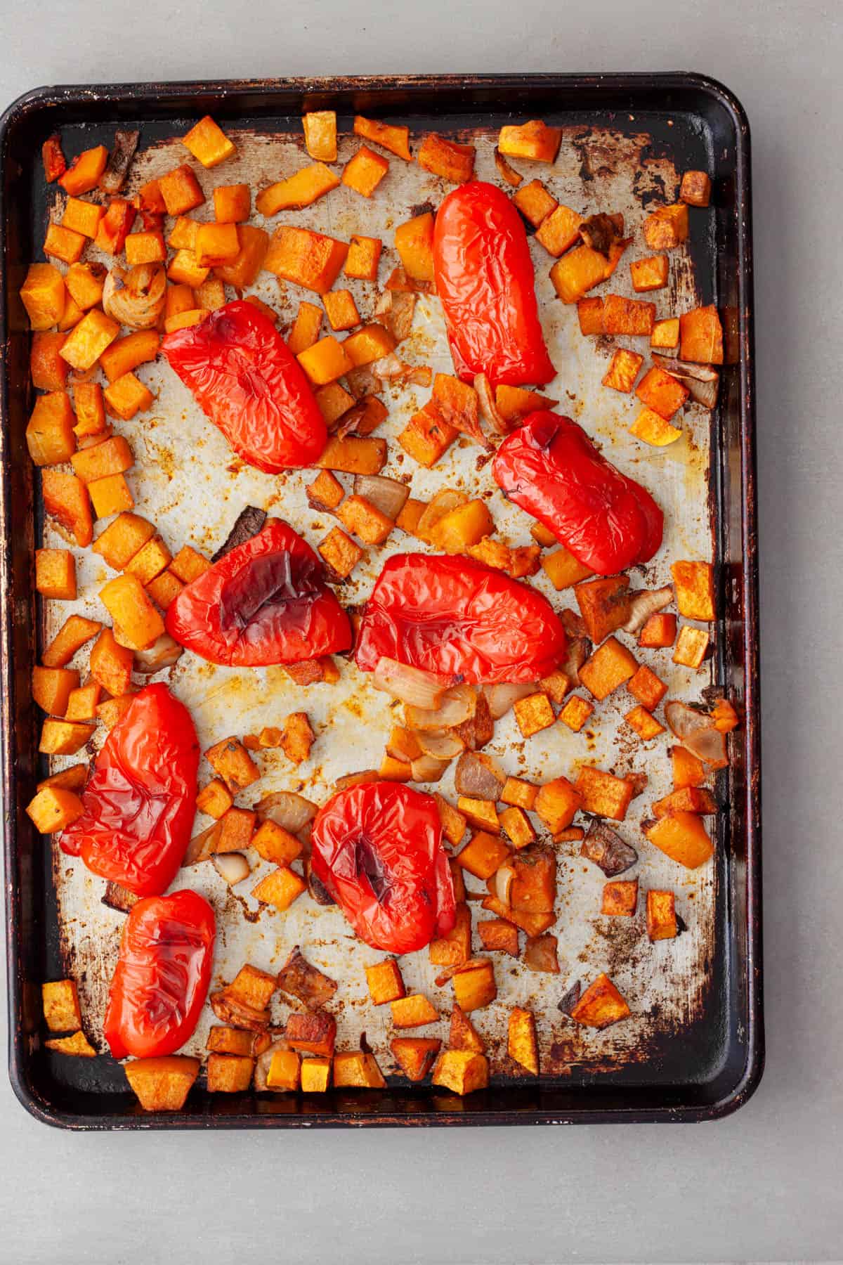 Roasted butternut squash, red peppers, onions and garlic on a baking sheet ready to be made into soup.