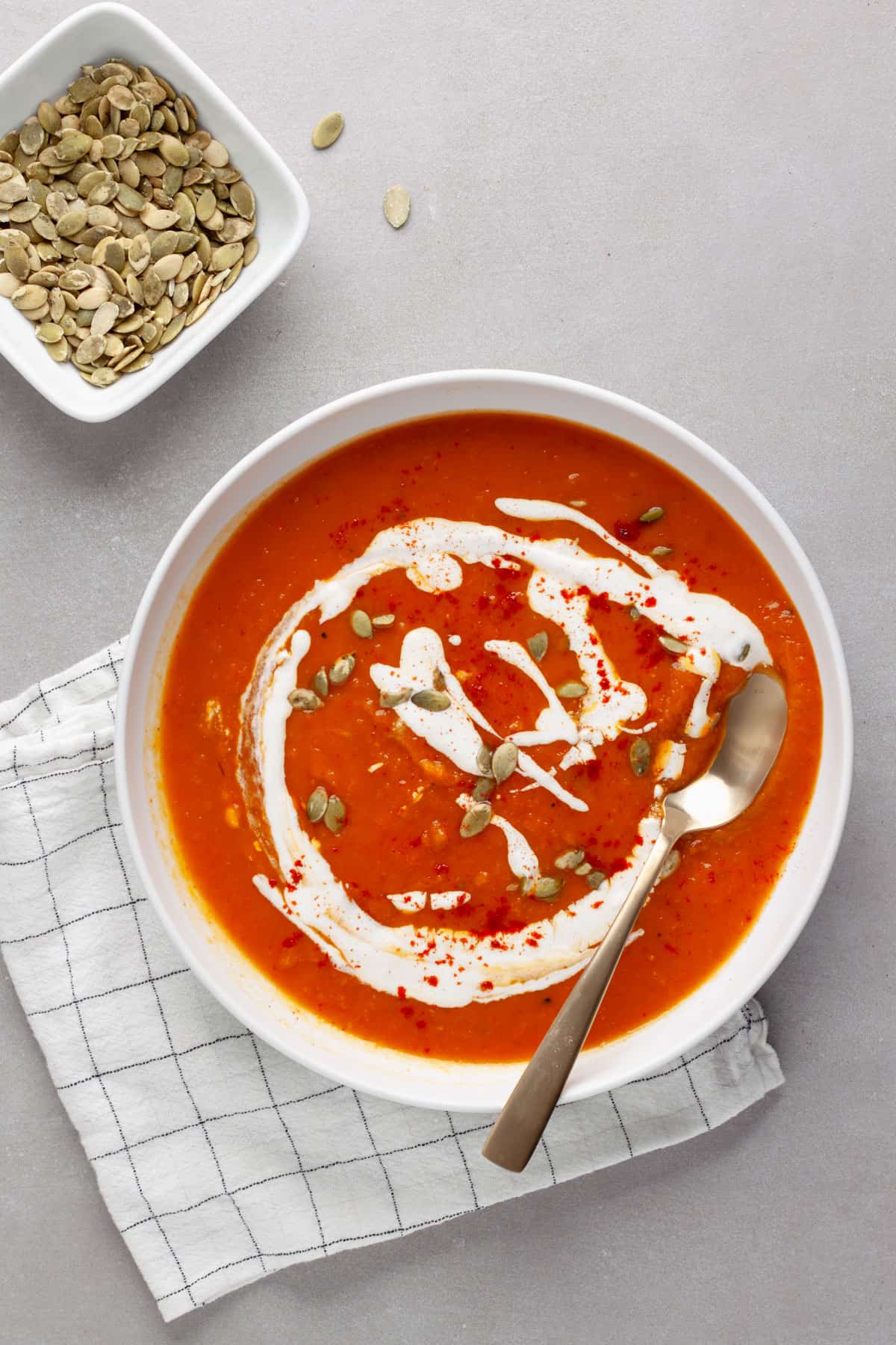 A bowl of butternut squash and red pepper soup topped with pepitas and sour cream.