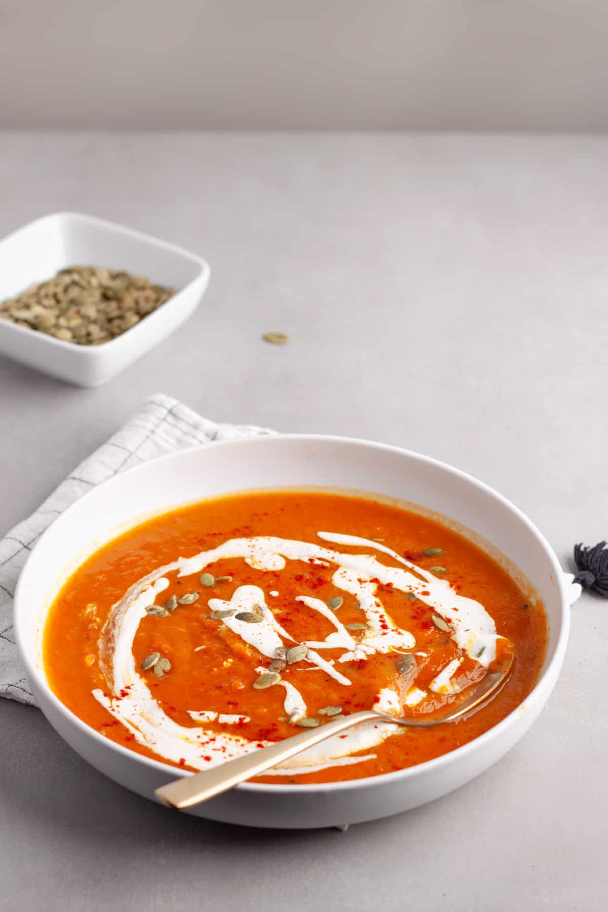 A bowl of butternut squash and red pepper soup garnished with sour cream, pepitas and paprika.