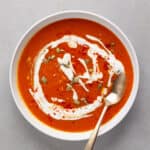 A bowl of butternut squash and red pepper soup topped with pepitas and sour cream.