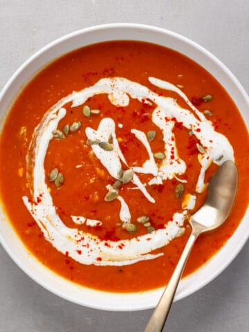 A bowl of butternut squash and red pepper soup topped with pepitas and sour cream.