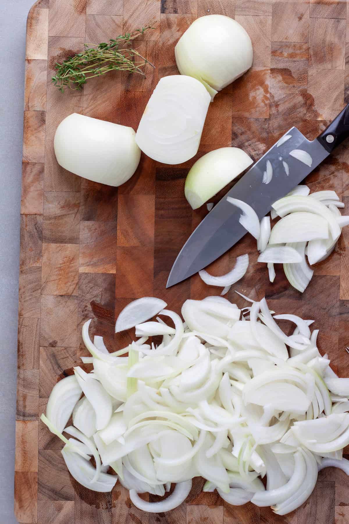 Onions getting sliced on a wooden cutting board ready to make caramelized onions.