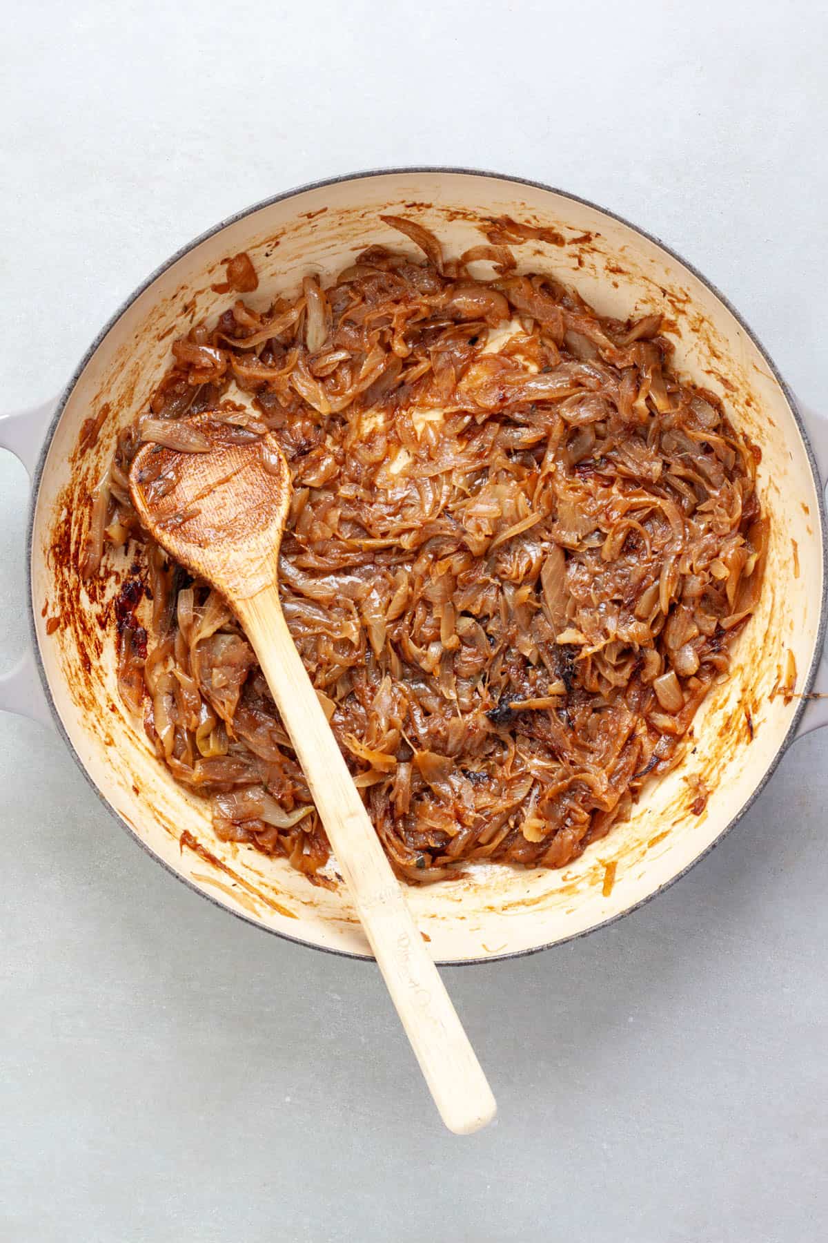 Caramelized onions freshly cooked in a large pan with a wooden spoon stirring them.