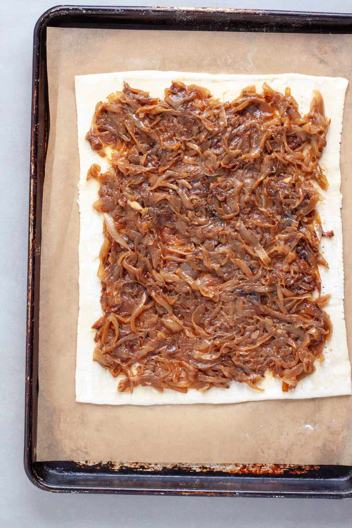 Caramelized onions spread in an even layer on a rolled out sheet of puff pastry.