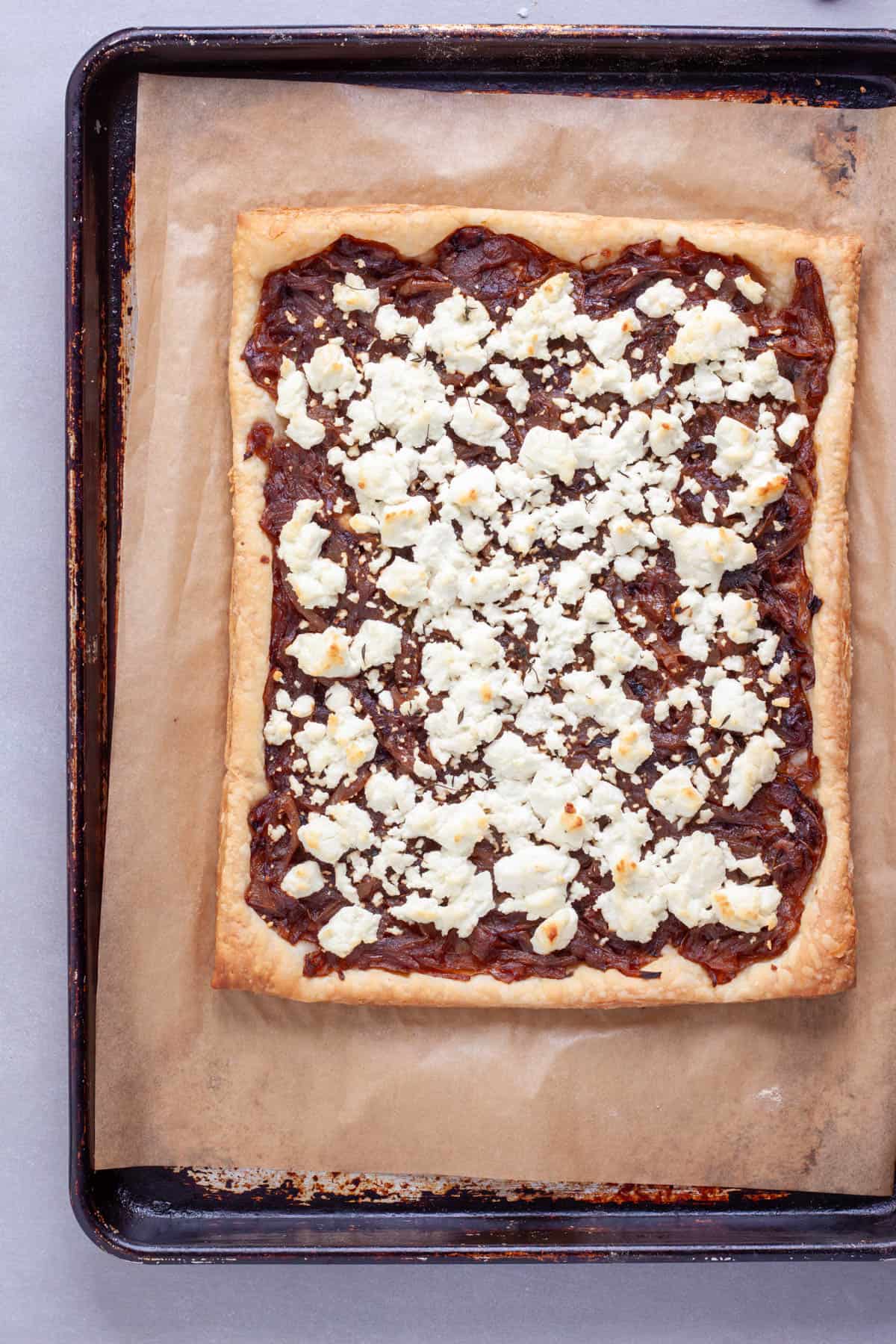 A cooked caramelized onions and goat cheese tart on a baking sheet.