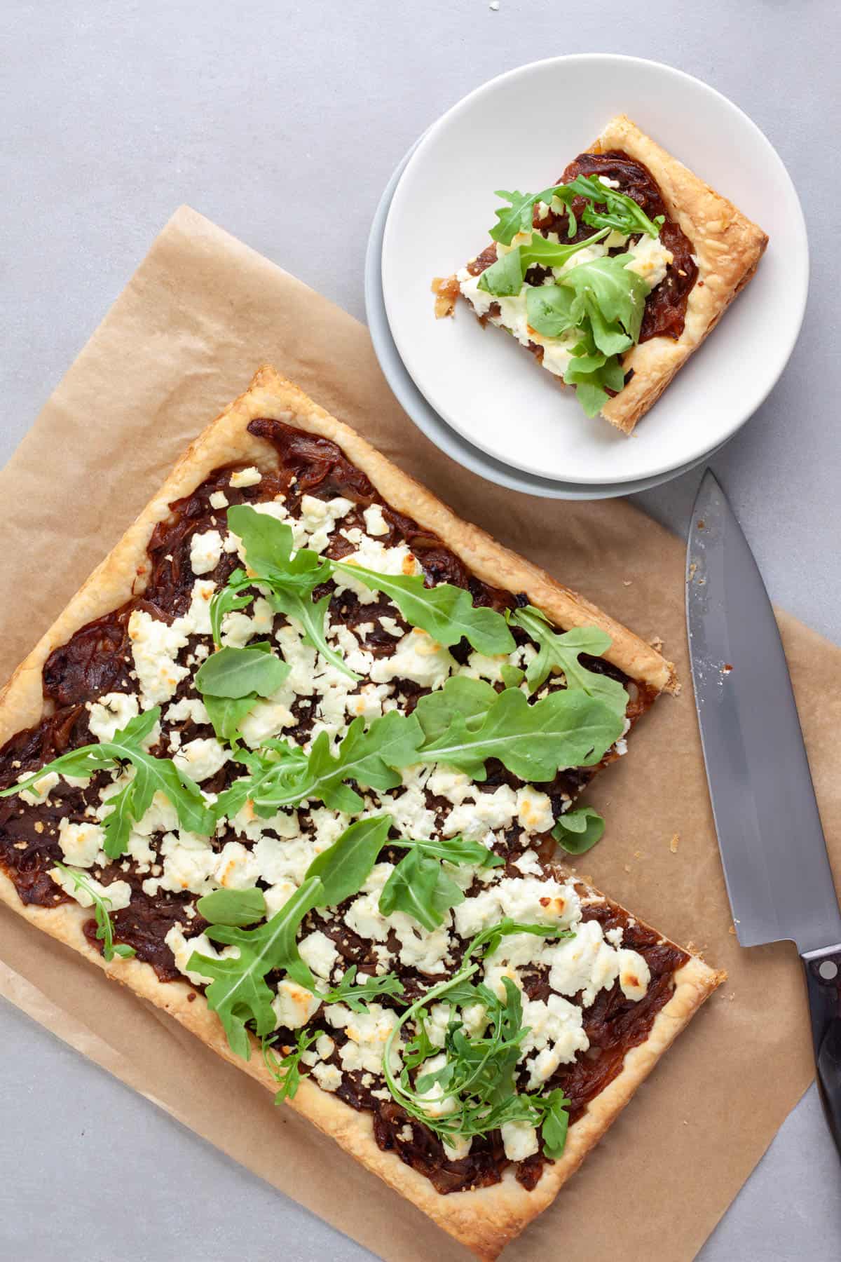 A portion of caramelized onion and goat cheese tart cut out of a larger tart and placed on a small plate.