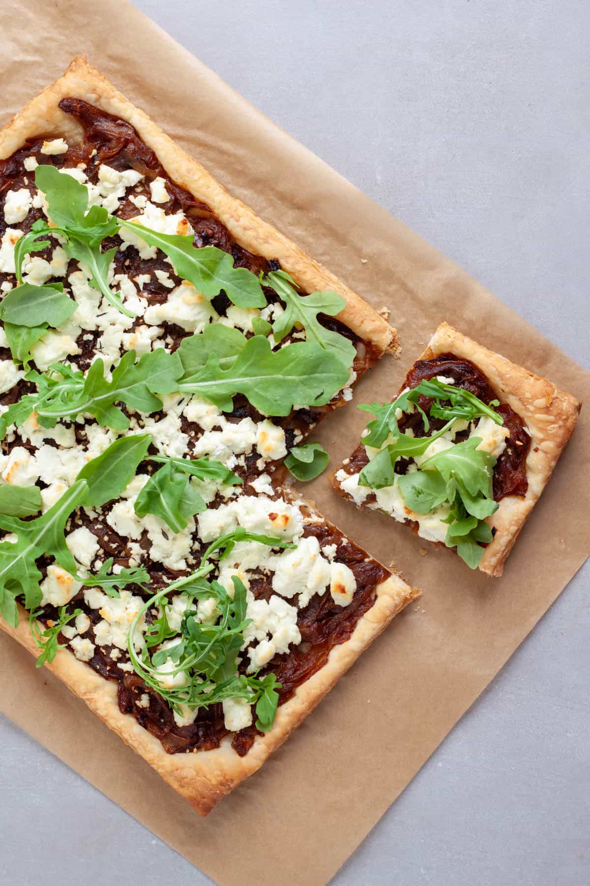 A caramelized onion and goat cheese tart on parchment paper with a portion cut out.
