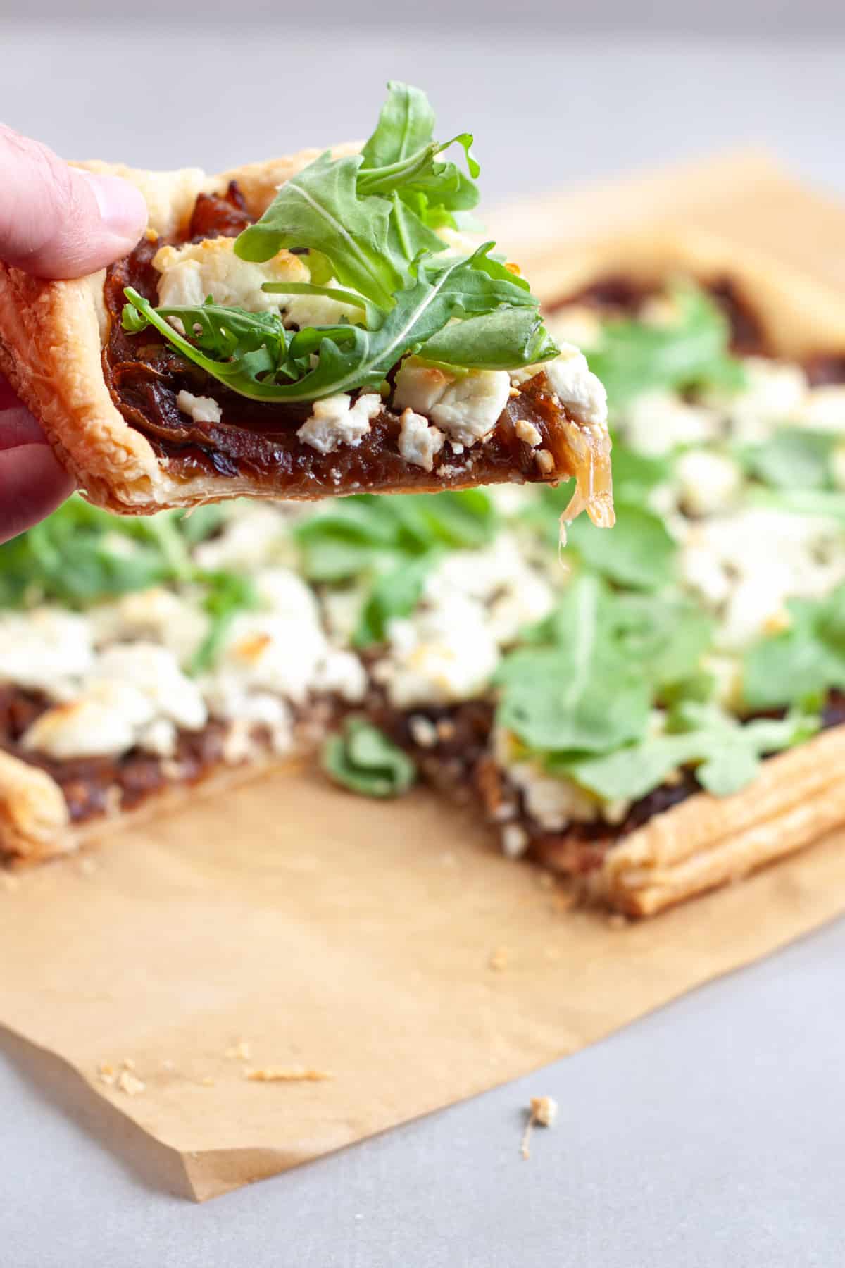 A portion of caramelized onion and goat cheese tart held by hand over the full tart.