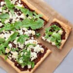 A caramelized onion and goat cheese tart on parchment paper with a piece cut away.