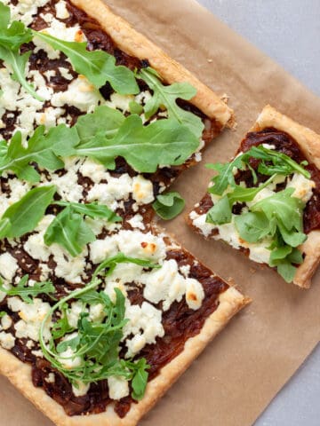 A caramelized onion and goat cheese tart on parchment paper with a piece cut away.