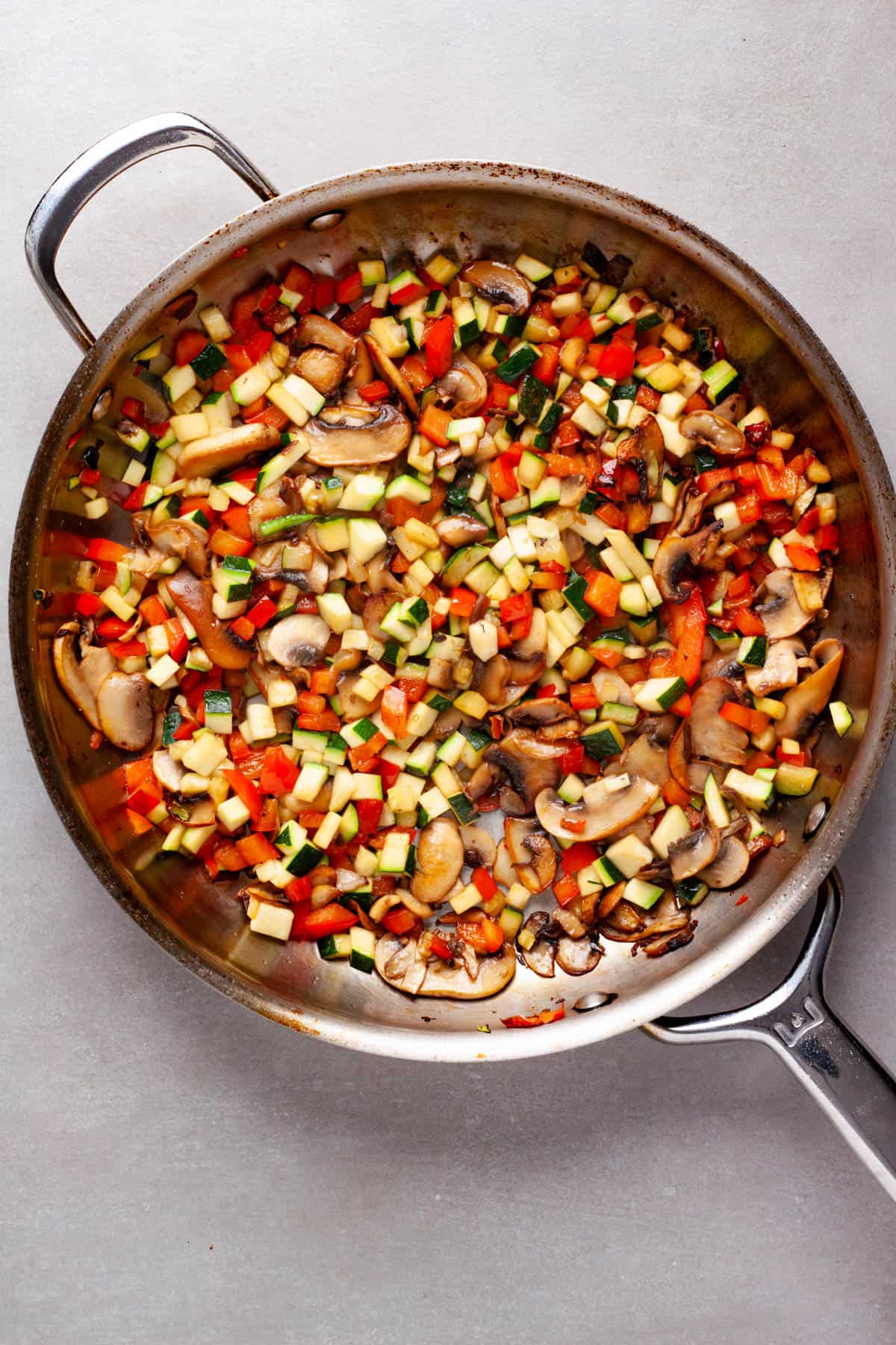 Peppers, zucchini and mushrooms cooking in a large skillet for a vegetable lasagna.
