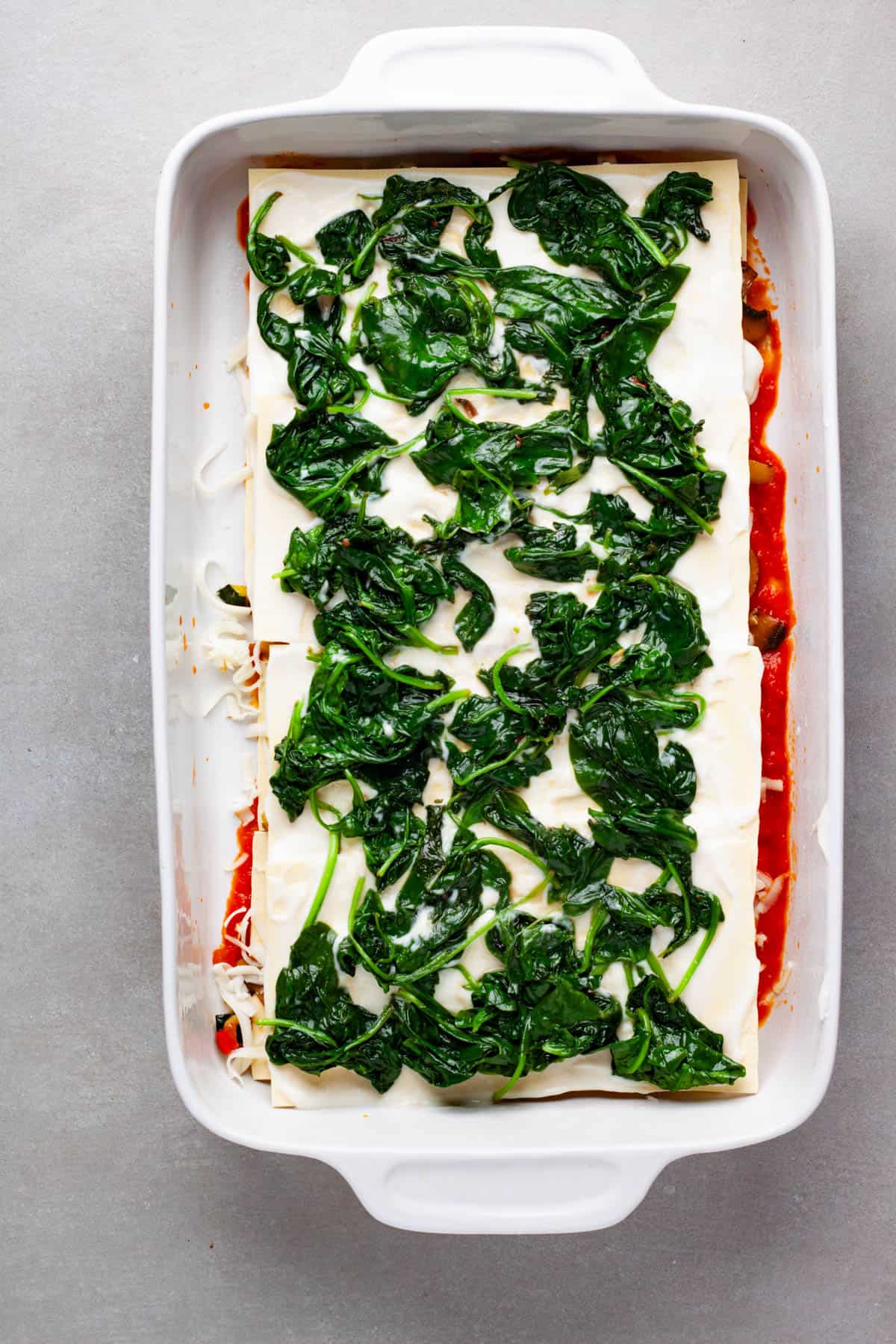 A bechamel and sauteed spinach added to lasagna noodles in a casserole dish.
