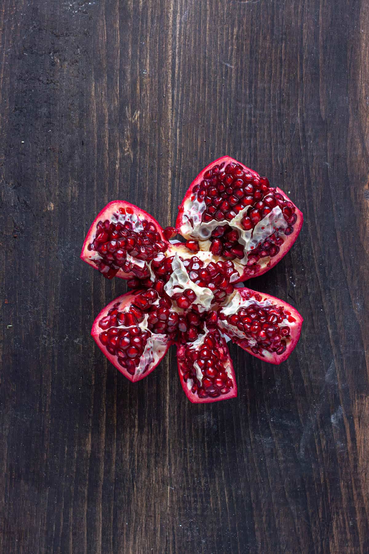 A pomegranate getting broken apart on a dark table.