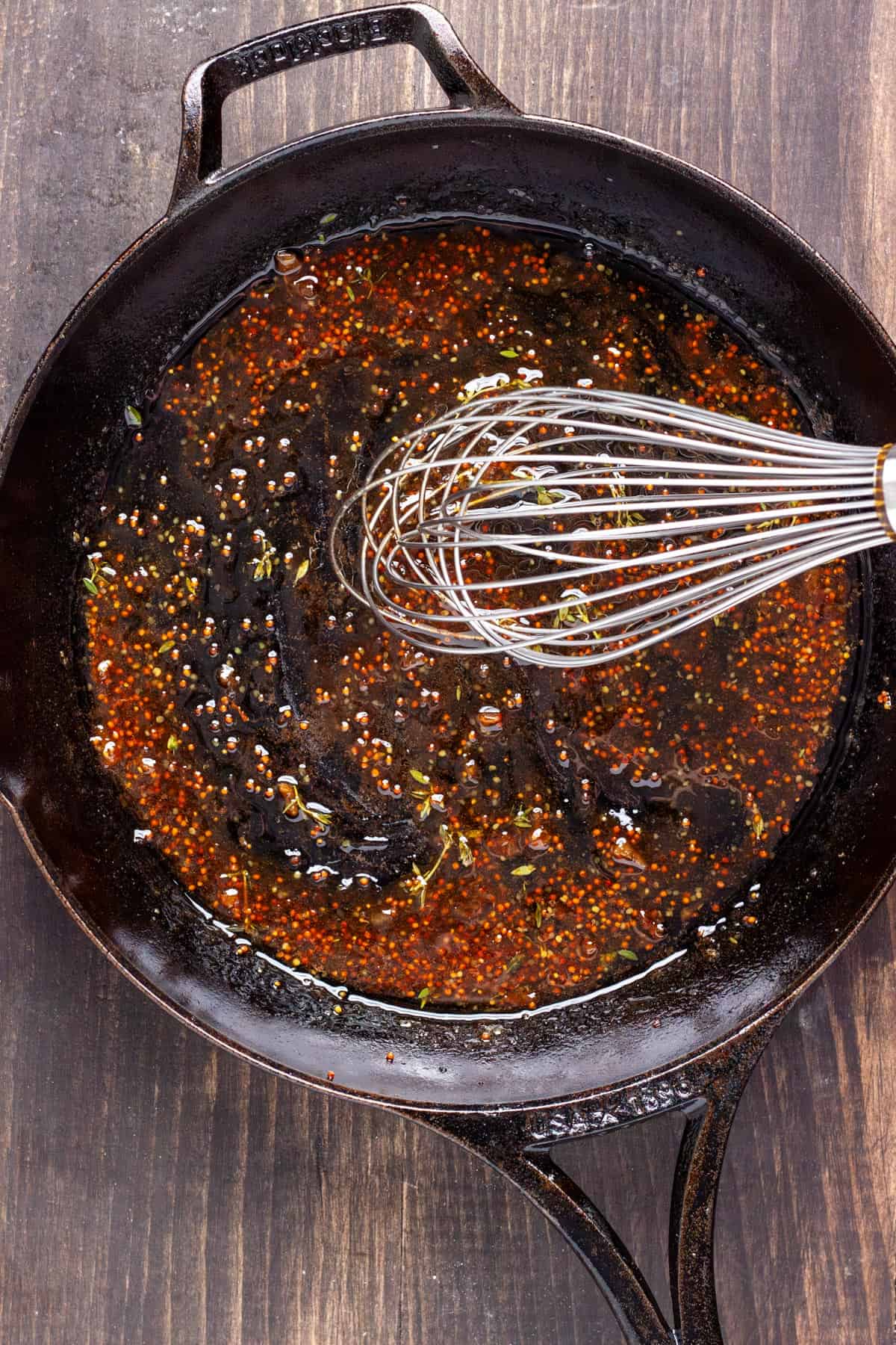 A bacon and fig jam dressing getting whisked together in a cast iron skillet.
