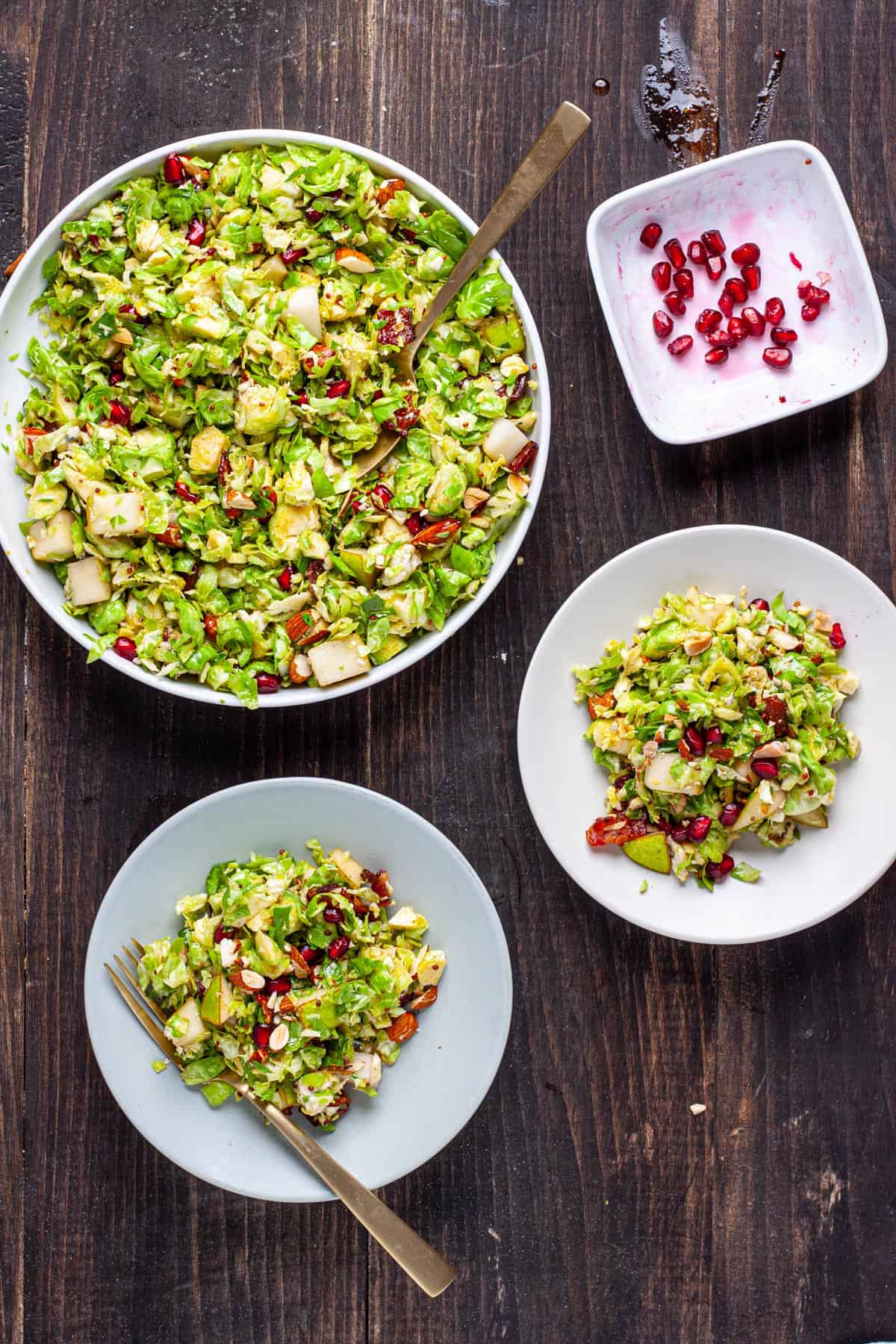 A large bowl of brussels sprouts salad with bacon and fig jam along with two servings on smaller plater on a dark table.