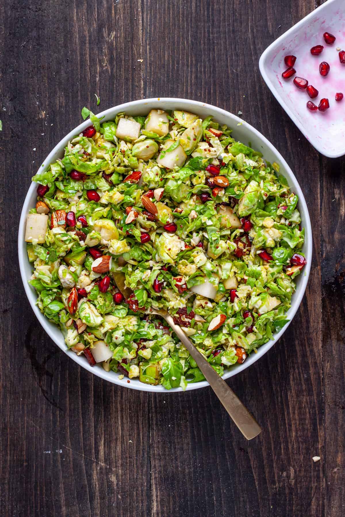 A serving platter of brussels sprouts salad with bacon and fig dressing and topped with pears and pomegranate arils.