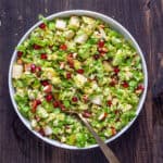 A serving platter of brussels sprouts salad with bacon and fig dressing and topped with pears and pomegranate arils.