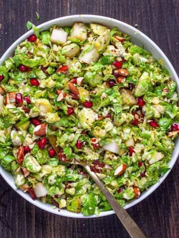 A serving platter of brussels sprouts salad with bacon and fig dressing and topped with pears and pomegranate arils.