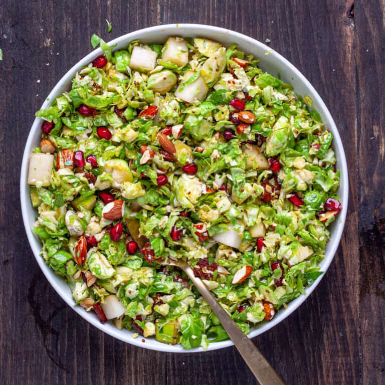 A serving platter of brussels sprouts salad with bacon and fig dressing and topped with pears and pomegranate arils.