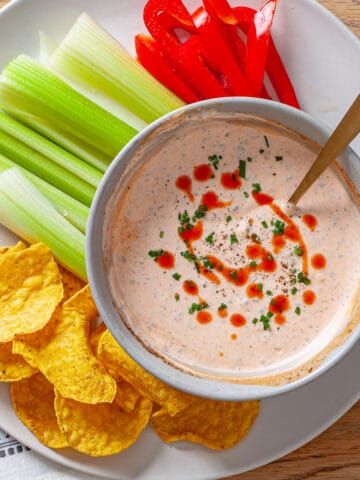 A bowl of homemade buffalo ranch sauce with cut vegetables and chips on a platter.
