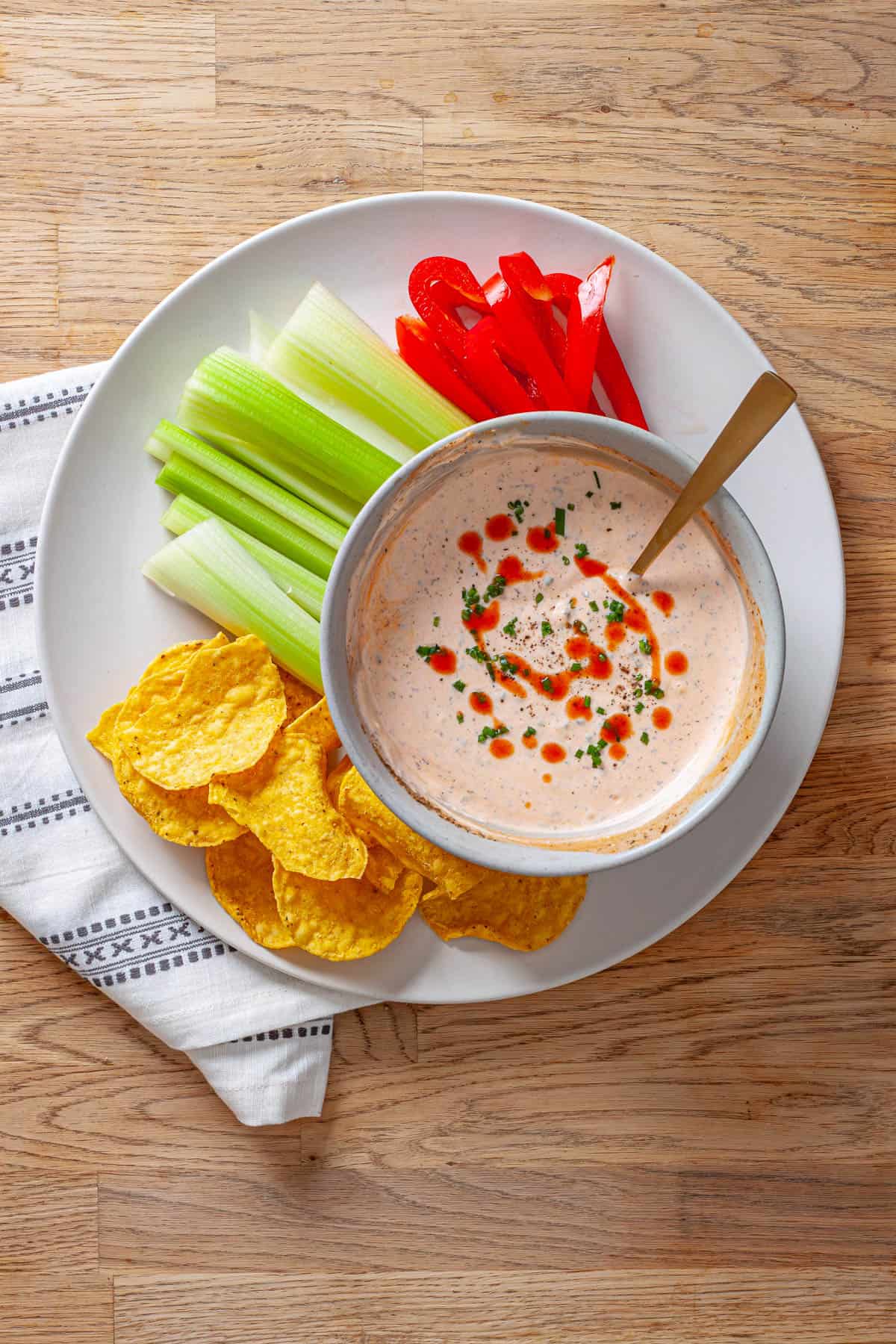 A bowl of homemade buffalo ranch sauce with cut vegetables and chips on a platter.