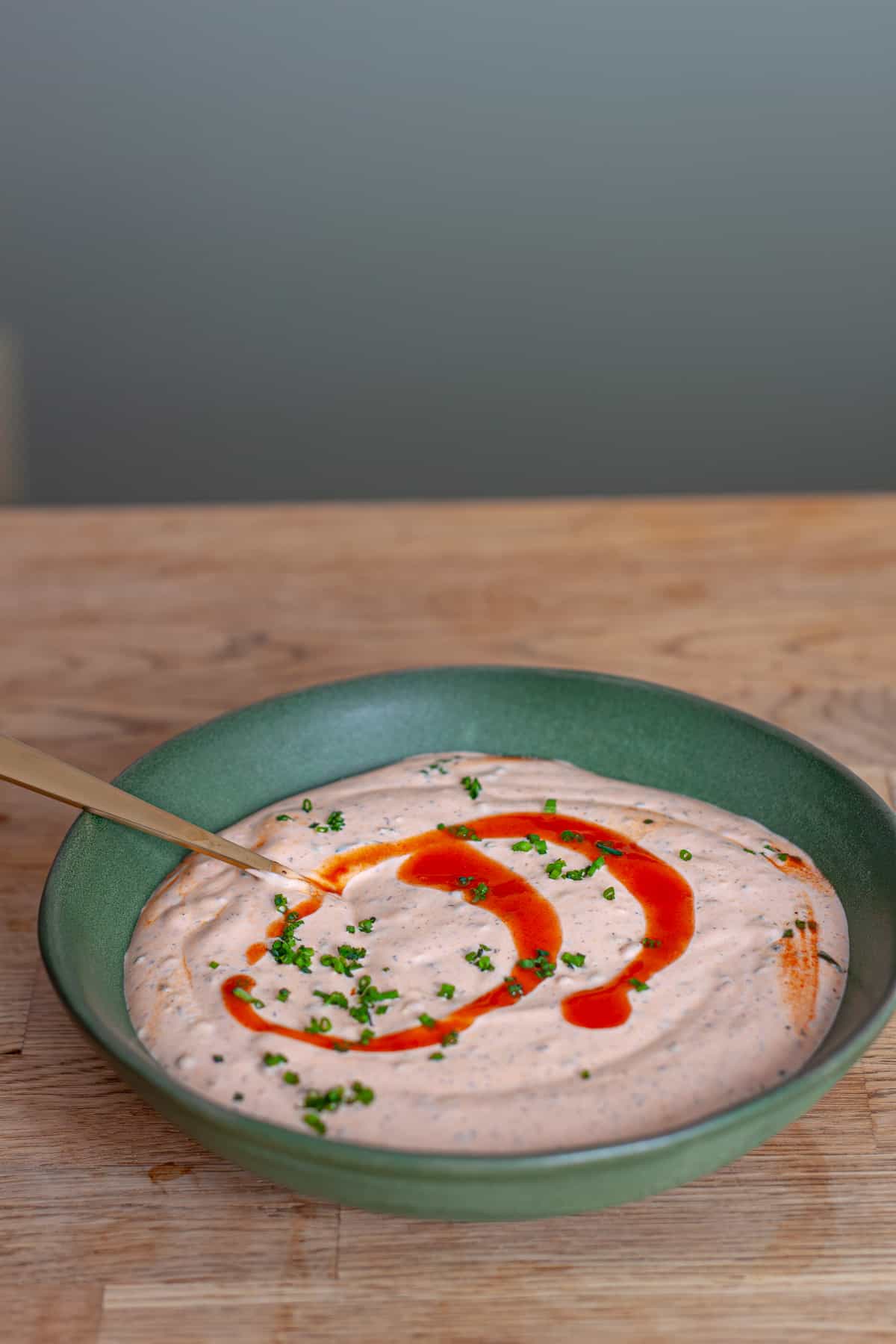 A green bowl with homemade buffalo ranch sauce garnished with chives and Frank's red hot sauce.