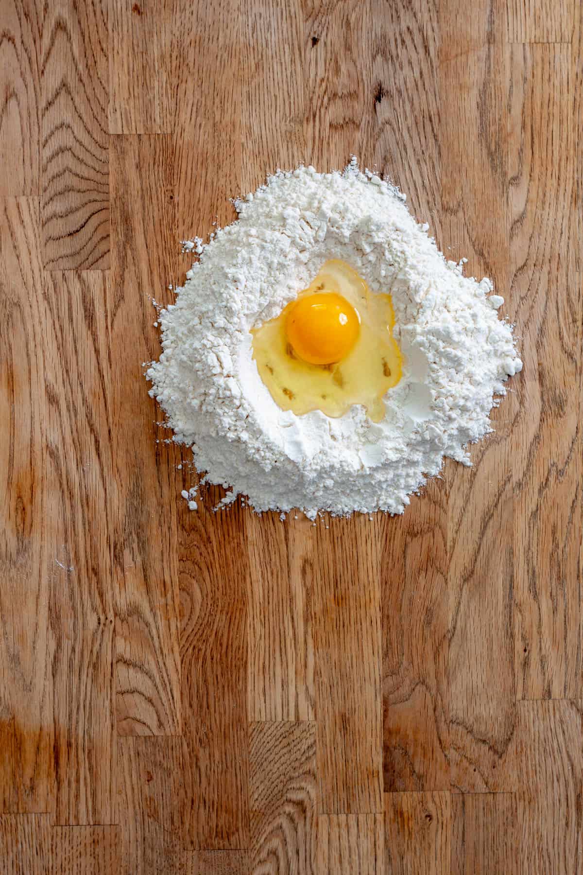 A mound of 00 flour on a countertop with an egg in the middle for fresh pasta.