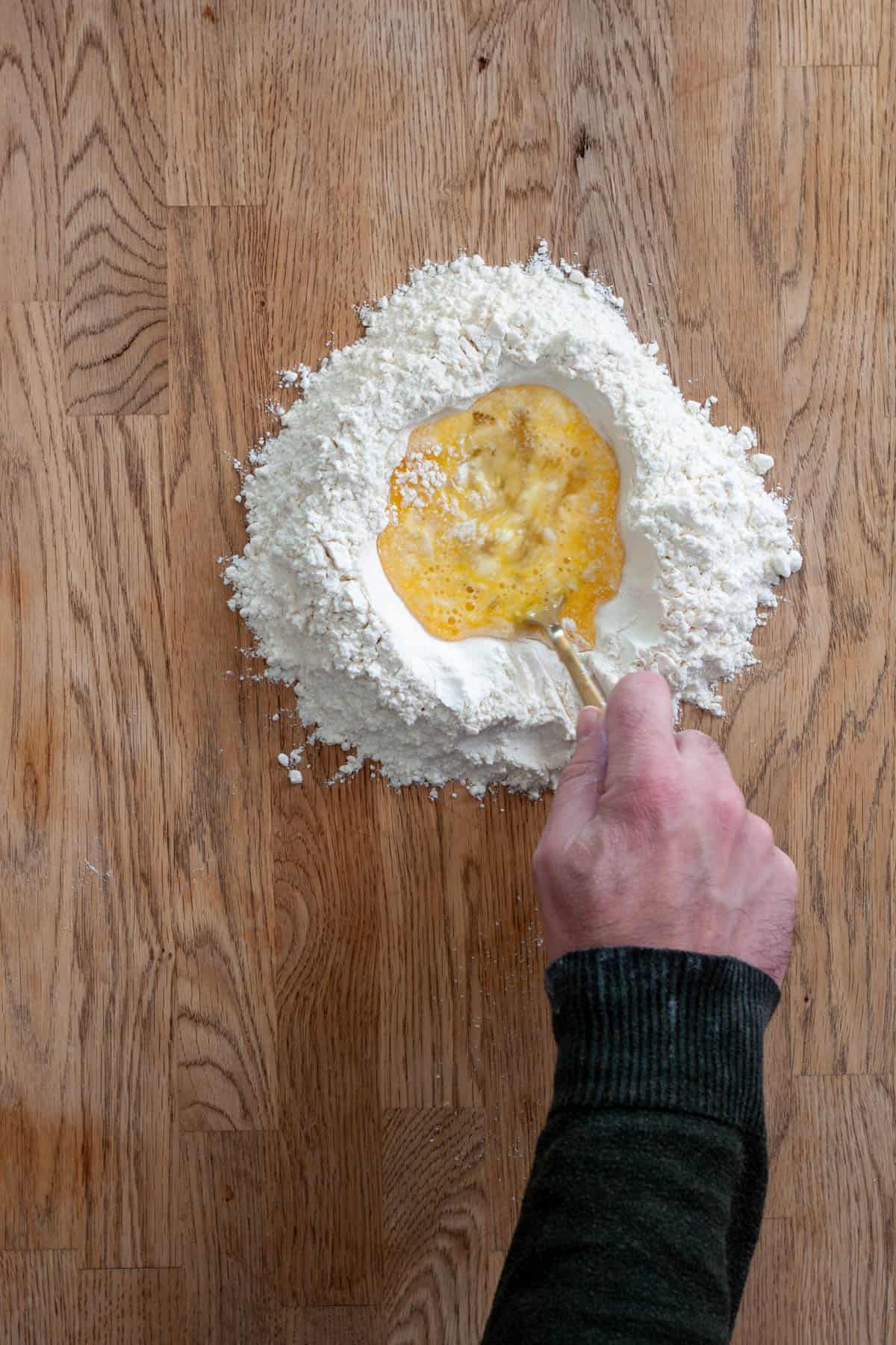 A fork whisking together an egg in the middle of a mound of flour for fresh pasta.