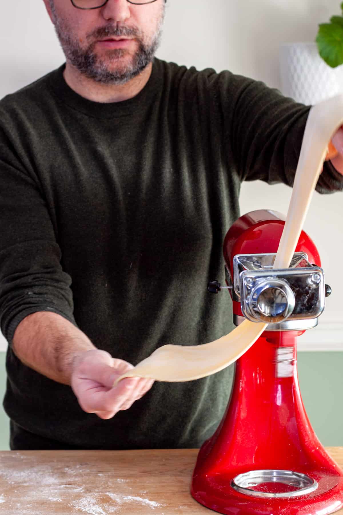A sheet of homemade fresh pasta rolling in a kitchenaid stand mixer with a pasta roller attachment.