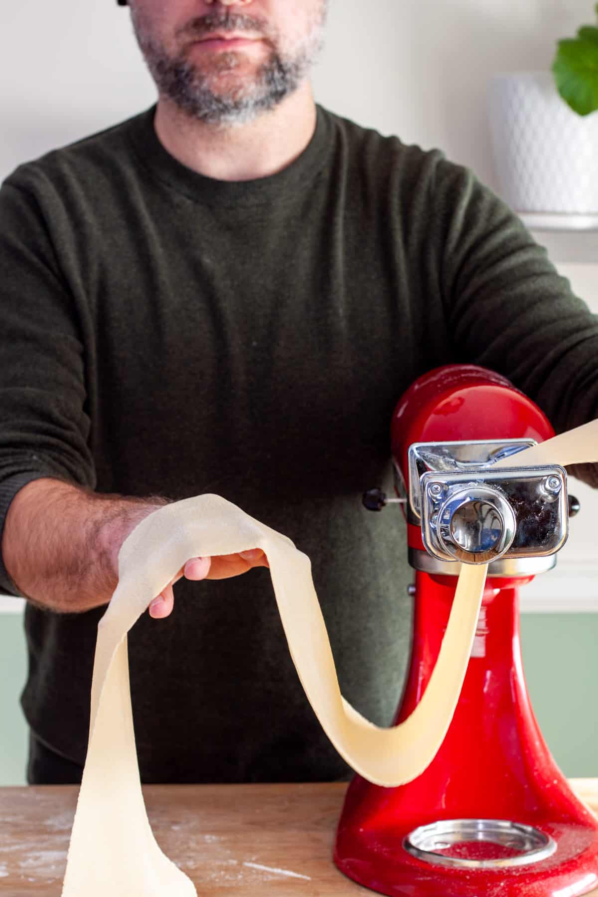 A sheet of homemade fresh pasta rolling in a kitchenaid stand mixer with a pasta roller attachment.