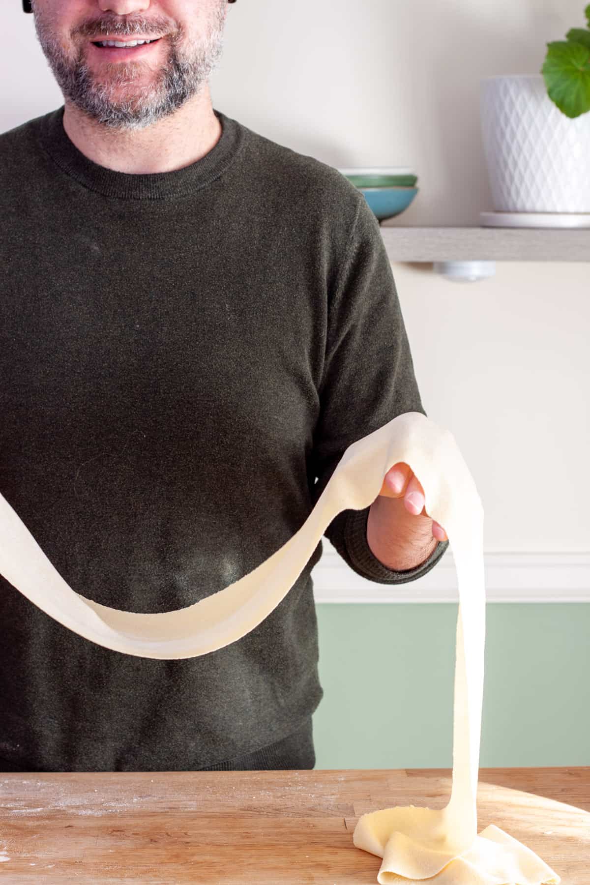Hands holding up a long sheet of homemade fresh pasta.