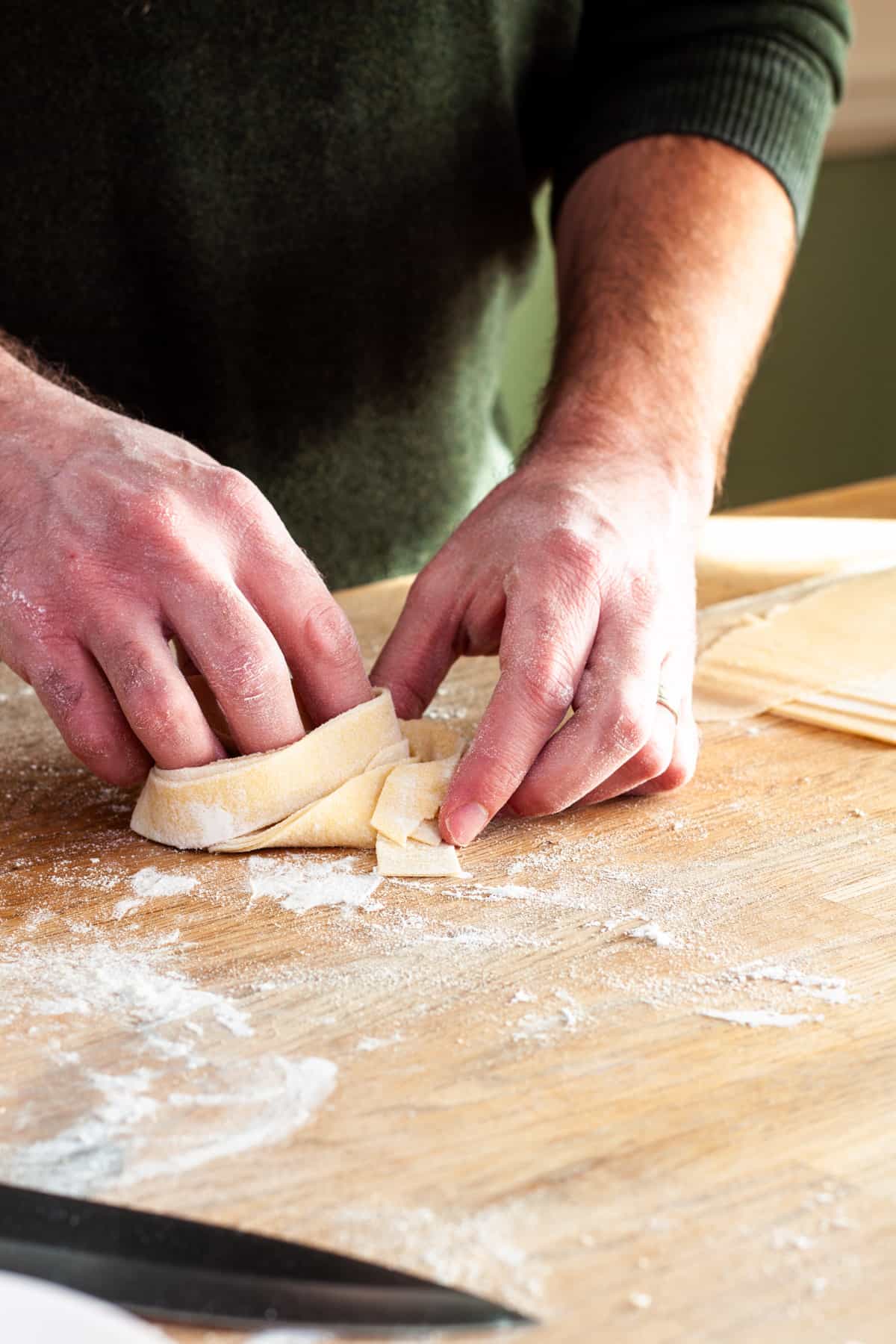 A nest of homemade fresh pappardelle getting turned together on a cutting board.