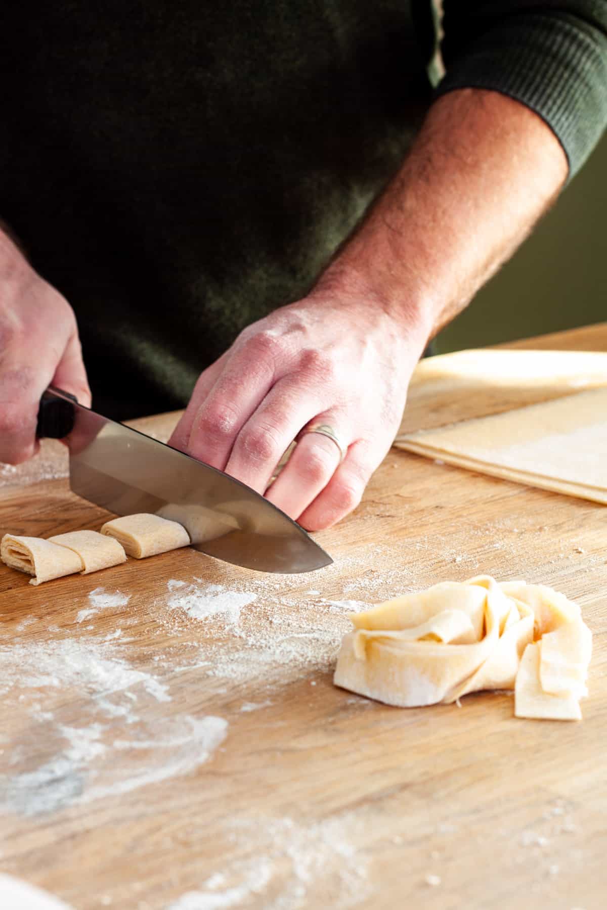 Rolls of fresh pasta getting cut for homemade pappardelle.