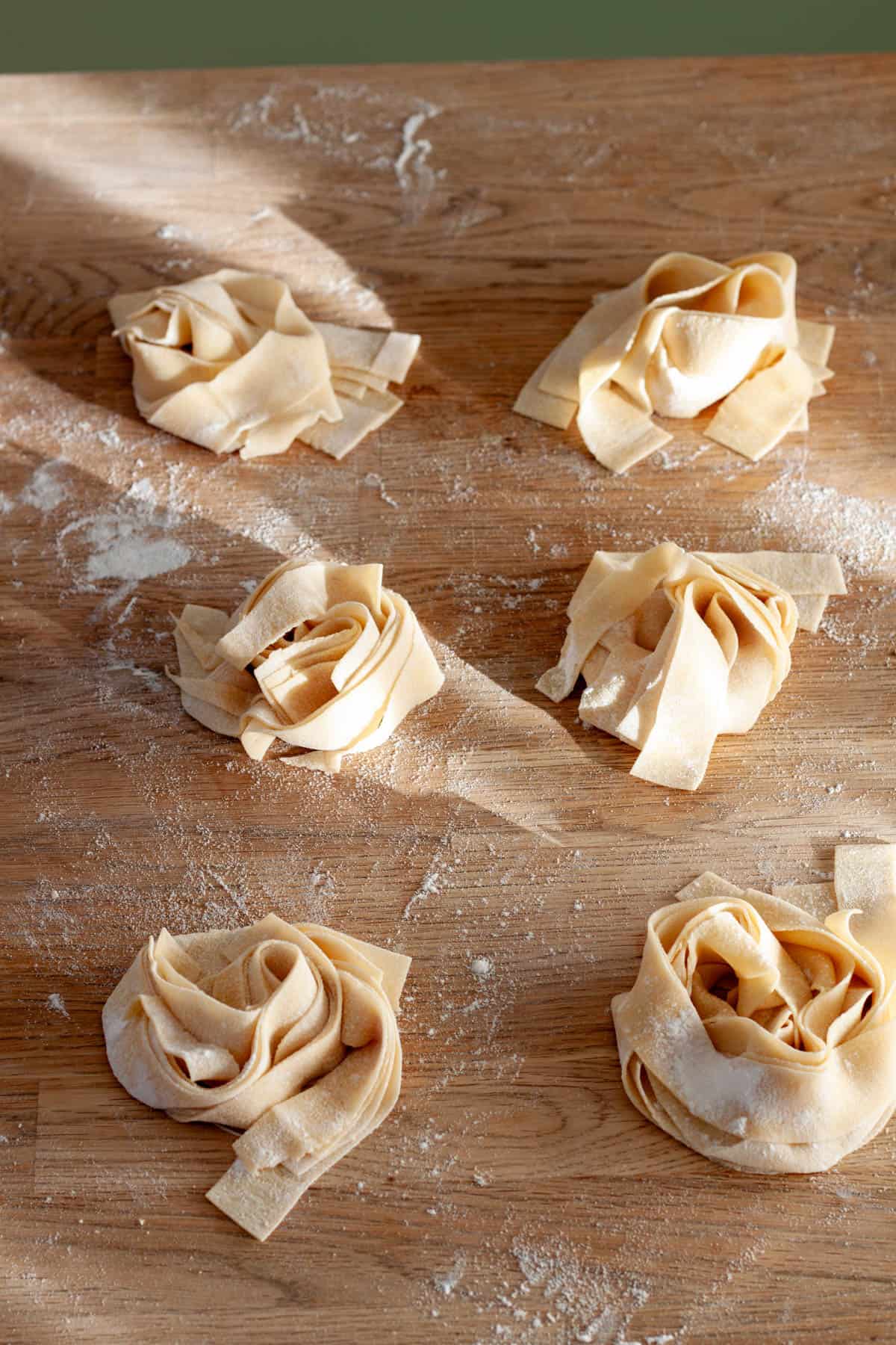 Mounds of homemade pasta on a butcherblock countertop.