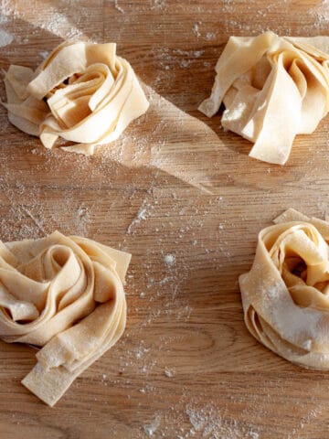 Nests of fresh homemade pasta on a butcherblock countertop.
