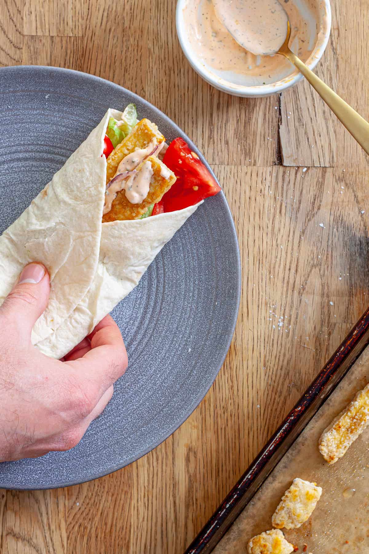 A crispy tofu wrap on a plate getting assembled.